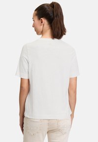 Witte t-shirt met korte mouwen, ronde hals en een gladde, lichte textuur. Heeft een kleine vlek tussen de schouders op de achterkant.