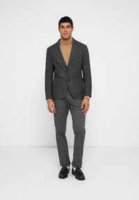 Gray tweed blazer with notched lapels, paired with a tan turtleneck and gray trousers. Black shoes complete the outfit.