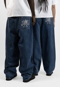 Denimjeans i mörkblått, oversized passform. Har broderade mönster på bakfickorna, med en blekt textur och subtila sömnadsdetaljer.