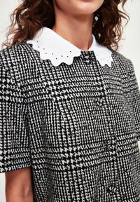 Zwart-wit hondenstoeth patroon jurk met een geschulpte witte kraag en knoopsluitingen, die een gestructureerde stof laat zien.