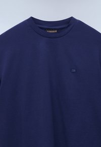 T-shirt bleu marine à col rond avec logo brodé discret sur la poitrine gauche et étiquette de marque visible à l'intérieur du col.