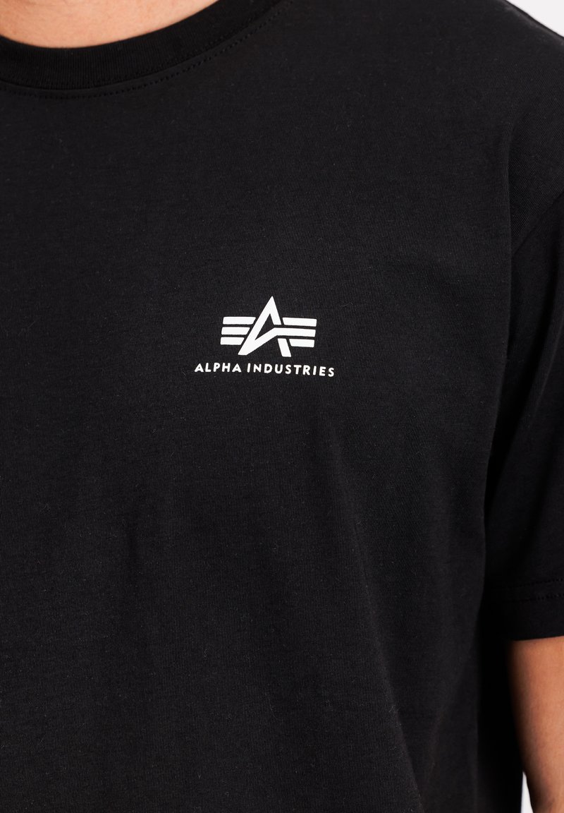 Czarna bawełniana koszulka z białym logo "Alpha Industries" oraz stylizowanym wzorem "A" na lewej piersi. Krótkie rękawy, okrągły dekolt.