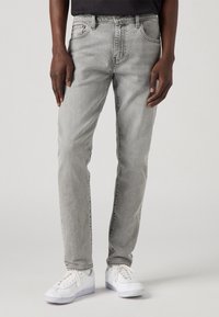 Szare dżinsy denimowe o prostym kroju, z pięcioma kieszeniami, delikatnym wyblaknięciem i detalami przeszyć; zestawione z białymi sportowymi butami.