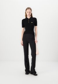 Polo noir à côtes avec des boutons dorés et une poche poitrine, associé à un pantalon évasé noir ; un sac à main rose clair complète le look.