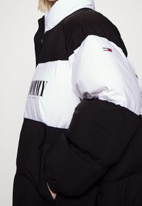 Giubbotto invernale con blocchi di colore bianco e nero, texture trapuntata, chiusura con zip e logo stampato sul davanti.