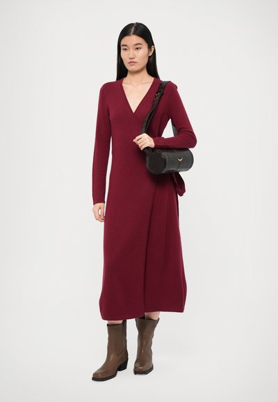Burgundy wrap dress with long sleeves, deep V-neckline, and a floor-length design. Paired with a black circular bag and brown ankle boots.