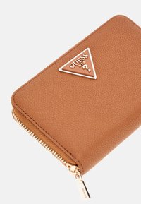 Portafoglio in pelle marrone con texture, logo triangolare dorato e chiusura con zip, caratterizzato da un design elegante e linee pulite.