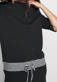 Top negro con un corte holgado, que presenta una cintura de rayas y un detalle de cordón. Tejido suave con mangas cortas. Diseño minimalista.