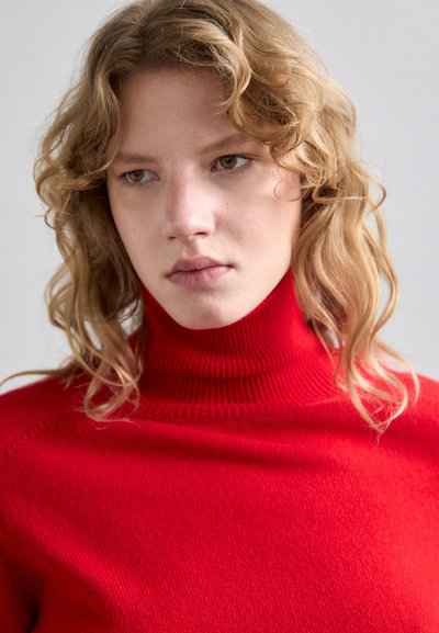 Punaiset turtleneck-neuleet, jotka on valmistettu neulottu materiaali, jossa on ribbireuna, ja jotka tarjoavat sileän tekstuurin ja tiukan muotoilun.