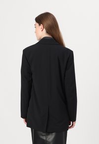Must kandaga blazer, millel on struktureeritud siil, sälgud ja külgventiilid, valmistatud siledast kangast. Stiliseeritud elegantse tagaküljega.