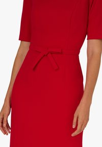 Czerwona sukienka z krótkimi rękawami, dopasowaną sylwetką i materiałowym paskiem w talii. Gładka tekstura i elegancki design.