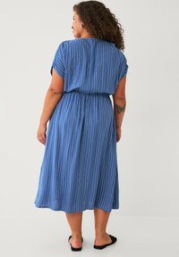 Abito midi a strisce blu con maniche corte, vita elasticizzata e gonna fluida. Realizzato in tessuto leggero, con una consistenza morbida e fessure laterali.