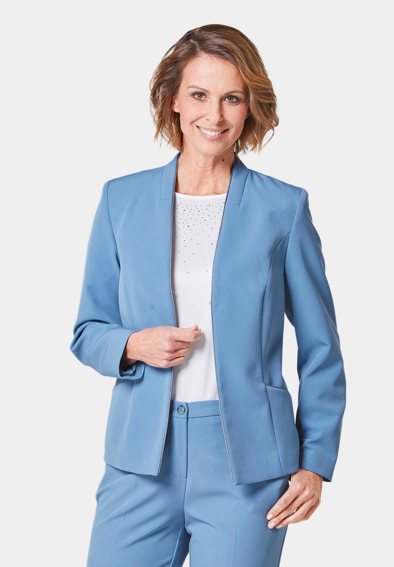 Lichtblauwe op maat gemaakte blazer van gladde stof, met een colless ontwerp en subtiele stiksels langs de randen. Draag het over een witte top.