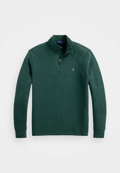 Zelený svetr s kulatým výstřihem vyrobený z strukturované látky. Má poloviční zip na límci a malé vyšívané logo na hrudi. Dlouhé rukávy.