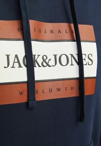 Hoodie bleu marine avec un grand motif blanc et marron portant les inscriptions "JACK & JONES" et "WORLDWIDE". Cordon de serrage et texture côtelée au bas.