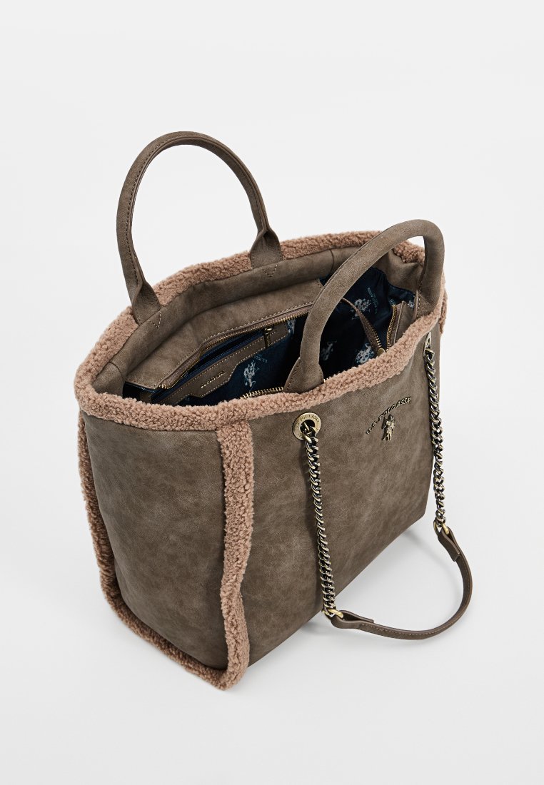 Sac fourre-tout en faux suède marron avec une bordure beige duveteuse, des poignées doubles et un intérieur bleu à motifs. Présente un détail en chaîne et des poches zippées.