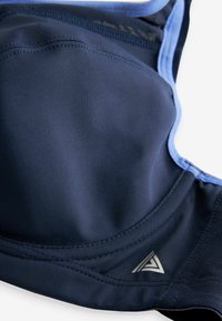Morska sportska grudnjak s glatkom tkaninom, kontrastnim svijetloplavim rubovima, podesivim trakama i srebrnim logotipom blizu dna.