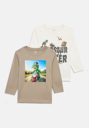 Două bluze pentru copii cu mânecă lungă, una bej cu un dinozaur care călărește o motocicletă, cealaltă albă cu diferiți dinozauri și textul "Puterea Dinozaurilor".