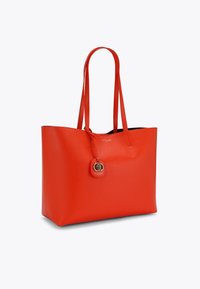 Czerwona skórzana torba tote z dwoma wydłużonymi uchwytami, otwartym topem, gładką fakturą oraz dekoracyjnym charms'em z złotym akcentem.