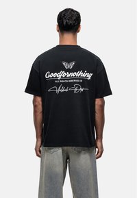 Czarna bawełniana koszulka z oversize'owym krojem, z białym napisem "Goodfornothing" oraz grafiką motyla na plecach. Luźny krój.
