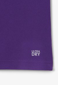 Paarse sportieve shirt van een textuurstof. Bevat een label aan de zoom met de tekst "ULTRA DRY" in zilver.