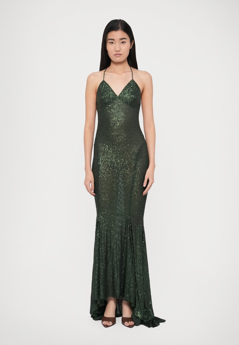 Ilga tamsiai žalia suknelė iš pailgučių, su kilpiniu kaklu, aptempta liemeniu ir praplatėjančiu kraštu. Lygi tekstūra ir blizgantys akcentai visame drabužyje.