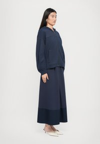 Felpa con zip color navy dal taglio oversize, dotata di tasche laterali, abbinata a una gonna a lunghezza caviglia con orlo inferiore a contrasto.