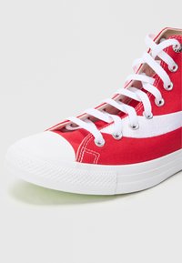 Raudonos drobinės aukštos kėdės sportbačiai su baltu guminio toe dangčiu ir padu, turintys baltas raištelius, akių angas ir šoninę baltą juostelę.