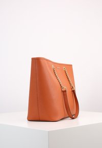 Borsa tote in finta pelle arancione con superficie testurizzata, accenti in catena e tracolla dorata, forma strutturata e design aperto.