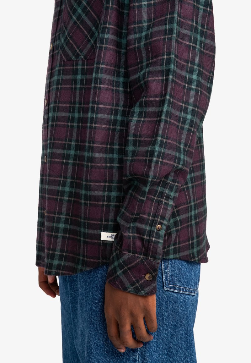 Camicetta a quadri bordeaux scuro e verde, realizzata in tessuto morbido, con taschino sul petto, polsini a bottone e un'etichetta cucita in basso.