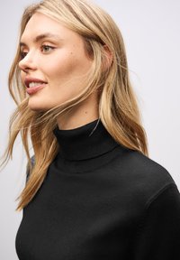 Maglione nero a collo alto con colletto a coste, realizzato in un tessuto a maglia liscia. Presenta una silhouette aderente e maniche lunghe.