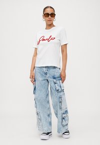 White cotton t-shirt with red "Smile" graphic, paired with light blue wide-leg cargo jeans with multiple pockets and black sneakers.