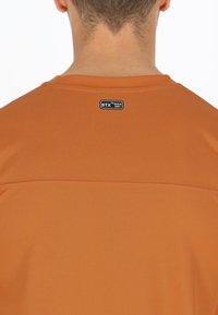 Hurtigtørrende, kortærmet skjorte i orange. Har et tekstureret stof med en rund halsudskæring og et logo-tag på ryggen.
