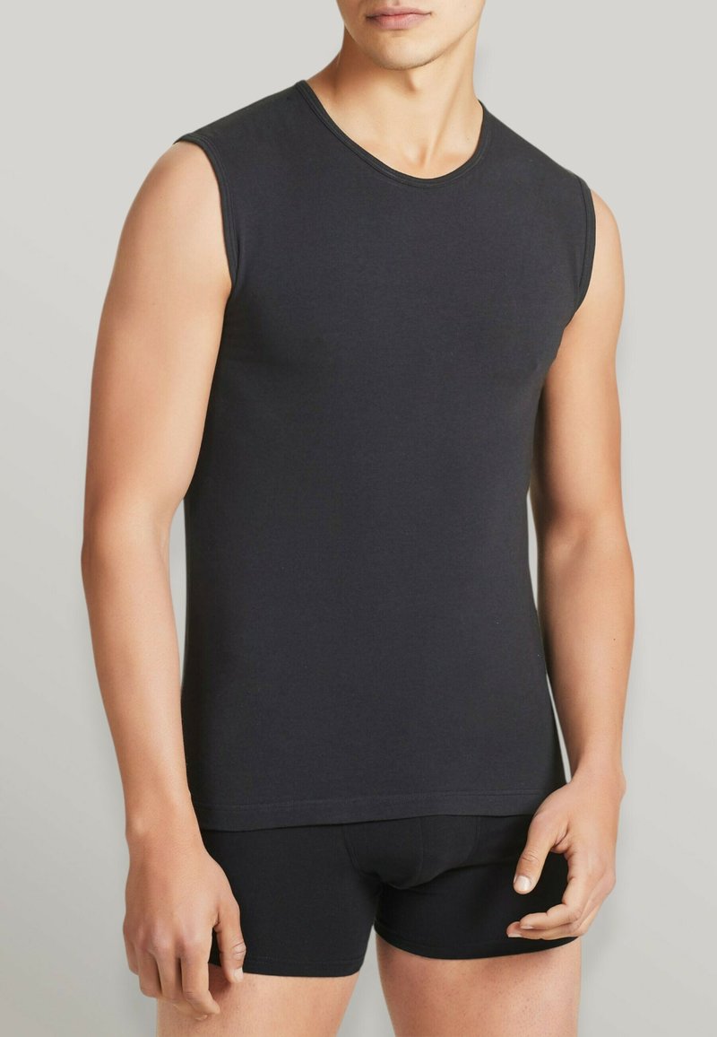 Top senza maniche nero in tessuto morbido con scollatura tonda, abbinato a pantaloni corti neri aderenti. Texture liscia e design minimalista.