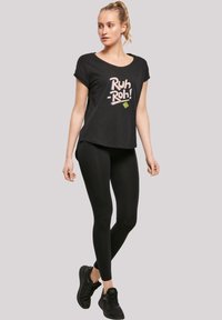Black T-shirt featuring the text "Ruh-Roh!" in colorful lettering, paired with black leggings and black athletic shoes.