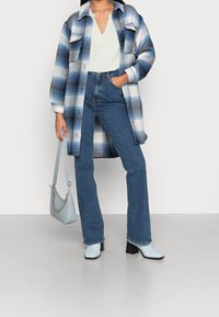 Giacca in flanella a quadri blu e bianchi, top verde chiaro, jeans blu a vita alta e stivaletti azzurri. Include una borsa azzurra.