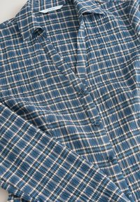 Modrá kockovaná košeľa vyrobená z mäkkej látky, s button-down prednou časťou, golierom a elastickou textúrou s kockovaným vzorom v tmavších odtieňoch.
