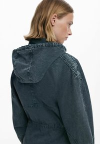 Tume teksajakk kapuutsiga, millel on tekstureeritud pind, nähtavad õmblused ja mugav lõige. Tagapoolne vaade näitab lihtsat ja kaasaegset disaini.