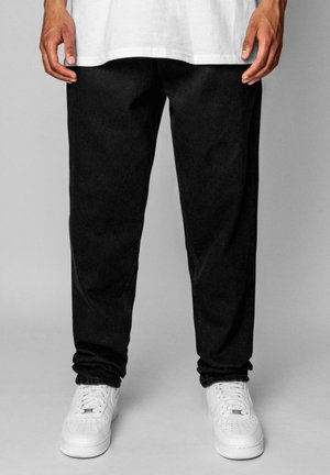 Black jogger pants with a relaxed fit, made of soft fabric, featuring a smooth texture, and paired with white sneakers.