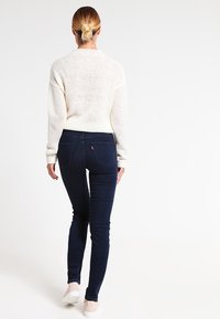 Lichtbeige gebreide trui, middelzware dikte, met geribbelde manchetten. Donkerblauwe skinny jeans, gladde textuur, met achterzakken en minimale details.