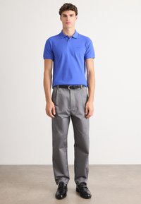 Polo azul de manga curta, calças cinzentas e sapatos pretos. O conjunto apresenta um corte clássico e um design simples.