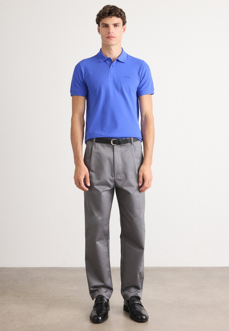 Niebieska koszulka polo z krótkim rękawem, szare spodnie oraz czarne buty. Strój ma klasyczny krój i prosty design.