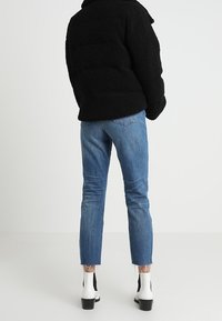 Sort fuzzy puffer-jakke, blå lige ben-jeans med frynsede kanter, og sorte og hvide ankelsko med blokhæl.