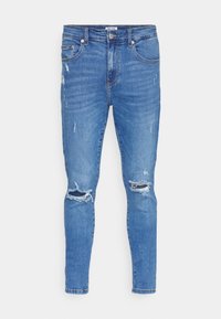 Vaqueros de mezclilla azul desgastados con un corte ajustado, que presentan detalles desgastados, rodillas deshilachadas, cinco bolsillos y cierre de cremallera.