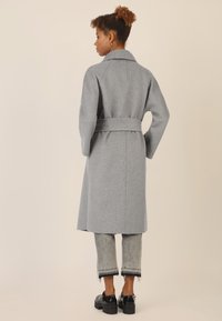 Cappotto di lana grigio con design dritto, vita con cintura e colletto ampio. Abbinato a pantaloni in denim accorciati e sfilacciati e scarpe chunky nere.