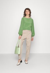 Blusa verde texturizada com mangas longas, calças bejes ajustadas e mala de ombro verde claro. Sapatos bicolores de biqueira quadrada completam o visual.