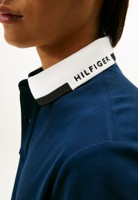 Polo navy con cuello blanco y detalles en negro, con "HILFIGER" bordado. Tejido suave con un diseño clásico.