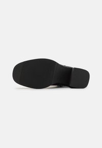 Svart såle med teksturert mønster, lett hevet hæl og glatt finish. Solid gummimateriale designet for grep.