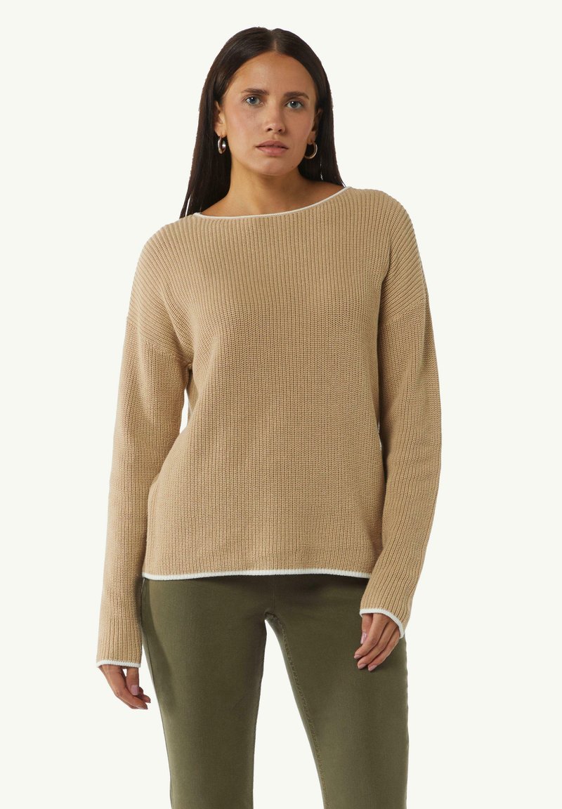 Beige, geribbelde sweater met lange mouwen, wijde halslijn en witte boord aan de onderkant. Gecombineerd met olijfgroene broek. Katoenmix stof.