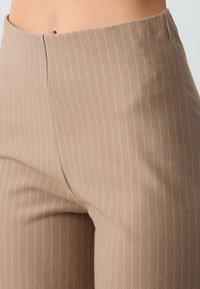 Lichtbruine gestreepte broek met een gladde textuur, voorzien van smalle witte streepjes en een hoge taille.